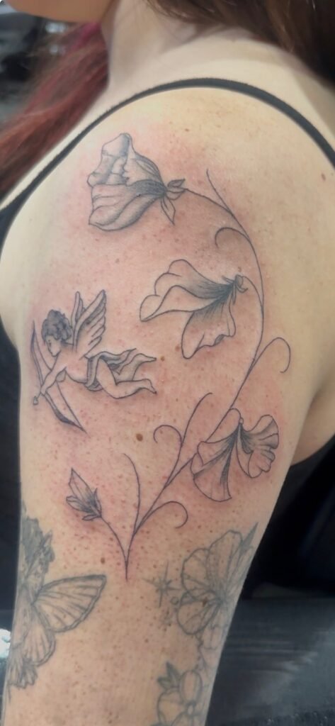 Fine-line sweet pea flowers and cherub shoulder tattoo by Monique Andujo